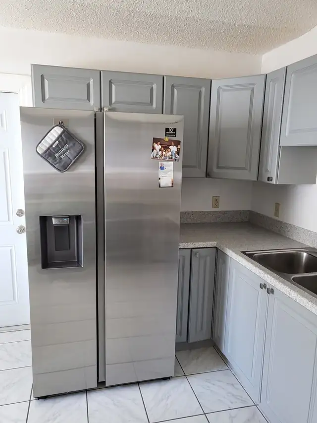 Grey kitchen cabinets and countertop next to a stainless side-by-side refrigerator