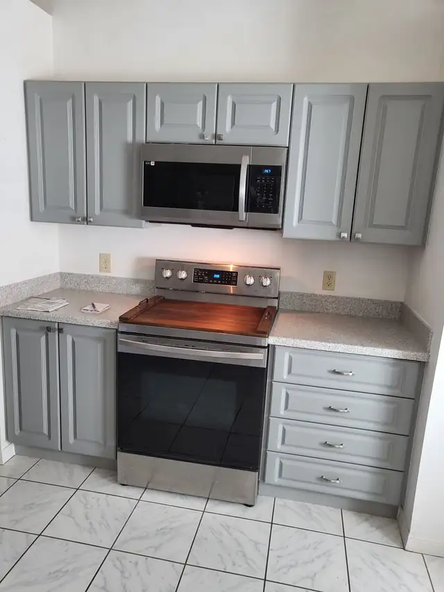 Grey raised-panel kitchen cabinets with a four-drawer stack, speckled grey countertop and stainless range