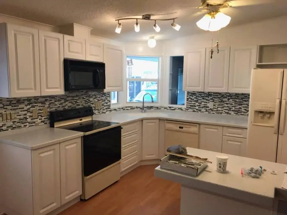 New kitchen cabinets in Lake Wales: white raised-panel cabinets, light countertops and a black and grey glass mosaic backsplash around a corner window